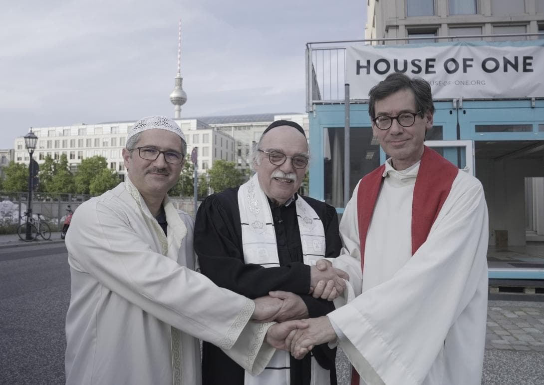 Vor der House of One-Box in Berlin-Mitte halten sich Imam Kadir Sanci, Rabbiner Andreas Nachama und Pfarrer Gregor Hohberg die Hände. ©Susanne_Bohlmann