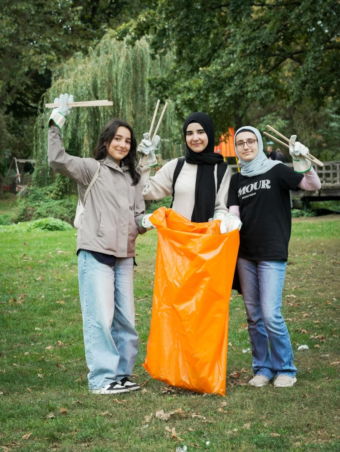 Drei Schülerinnen, die gemeinsam mit dem House of One am Clean up-Day, in einem Berliner Park Müll sammeln.