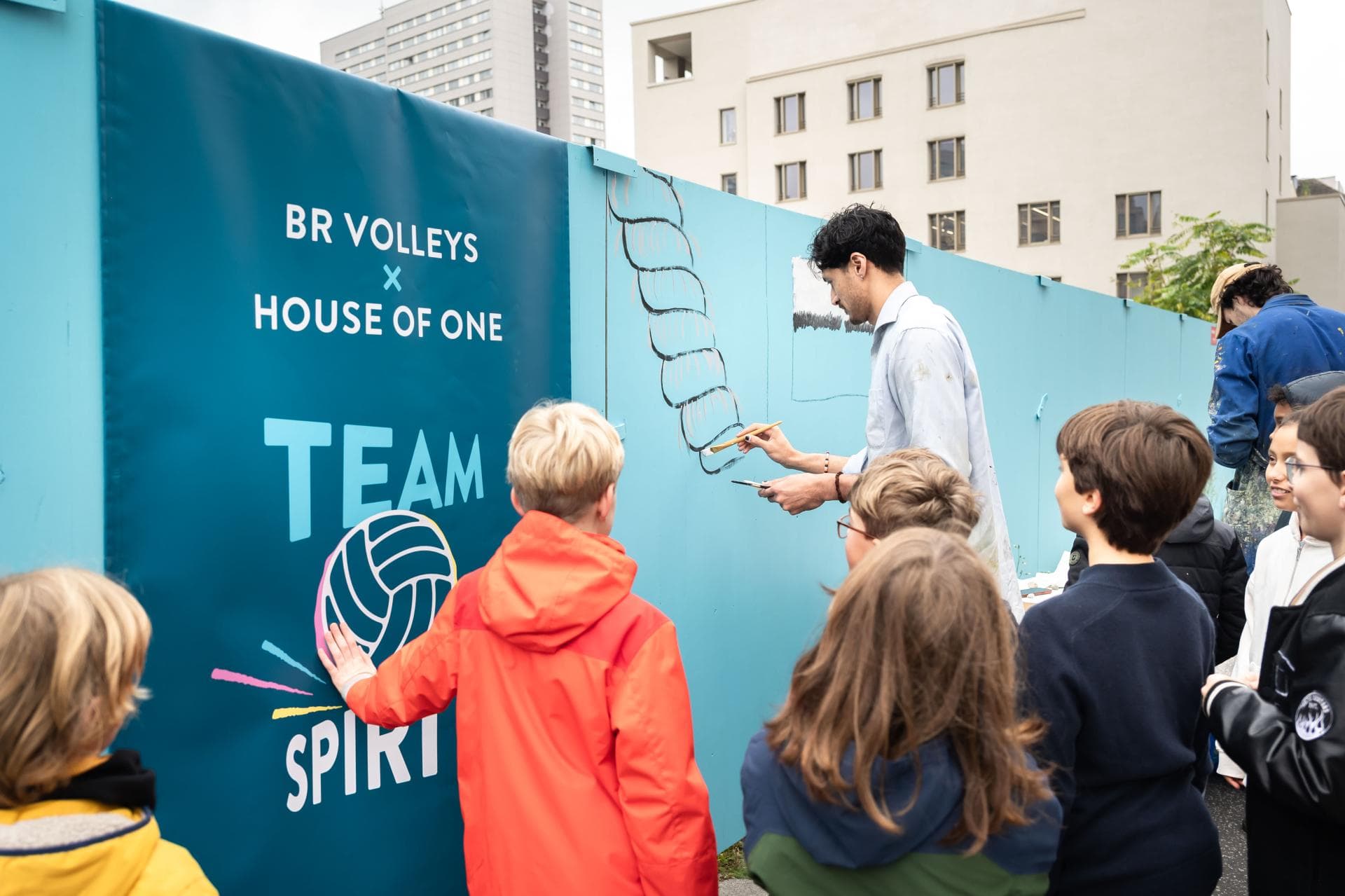 Nehemiah Mote, BR Volley-Profi, malt ein aus mehreren Seilen gedrehtes Tau auf den Bauzaun des House of One. 